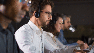 A row of technical support agents wearing headsets, working intently at computers in a dimly lit office. Represents IT support for businesses and IT support services, highlighting professional helpdesk teams available for remote or onsite support in locations such as Miami.